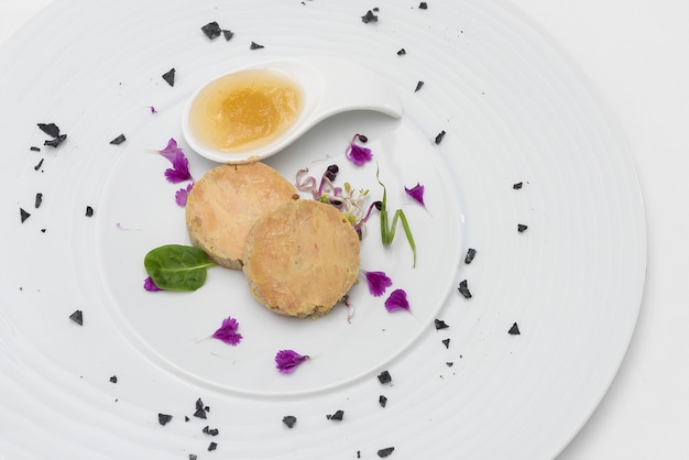 Terrine de foie servie avec une sauce sucrée, décorée de pétales de fleurs et de feuilles vertes