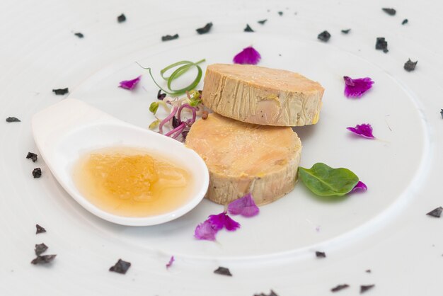 Terrine de foie servie avec une sauce sucrée, décorée de pétales de fleurs et de feuilles vertes