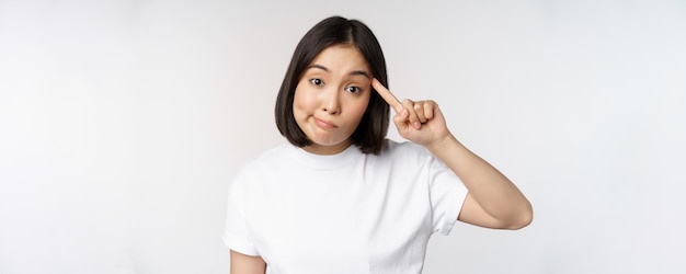 Êtes-vous fou Jeune femme asiatique rouler le doigt sur la tête se moquant de quelqu'un de stupide debout en t-shirt sur fond blanc