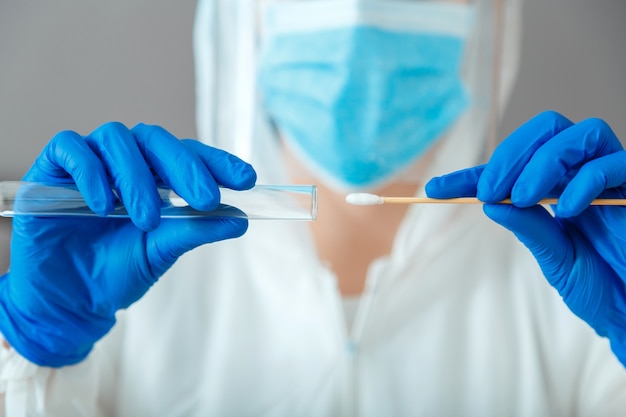 Test Covid 19 pcr dans les mains des infirmières. Docteur en combinaison de protection gants de masque médical tenant un échantillon de salive d'écouvillon pour le diagnostic du virus du coronavirus covid19 en laboratoire. Test PCr de culture nasopharyngée. Fermer