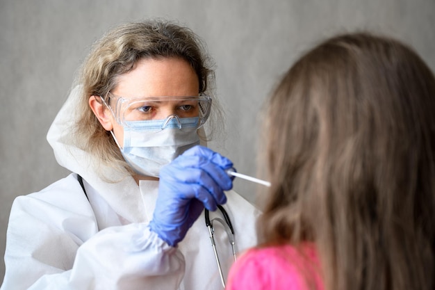 Test COVID19 dans une clinique, un médecin tient un écouvillon pour un échantillon de mucus d'un enfant