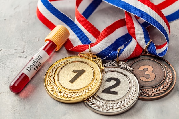 Test de dopage. Médaille d'or, d'argent et de bronze et tube à essai avec du sang sur une surface grise.