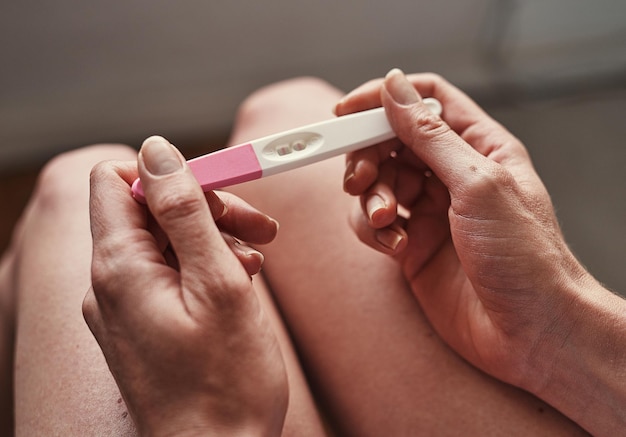 Test de grossesse mains et femme avec des résultats enceintes dans son appartement ou maison avec un résultat positif Planification du bébé et de la personne ou de la mère avec un bâton de test de maternité pour la confirmation de la fertilité