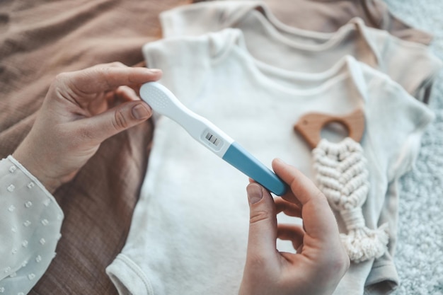 Test de grossesse positif sur le fond de jolis vêtements de bébé