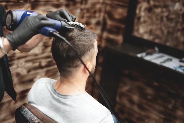 Tête de coupe de cheveux dans un salon de coiffure. Le coiffeur coupe les cheveux sur la tête du client. Le processus de création de coiffures pour hommes. Salon de coiffure. Mise au point sélective.