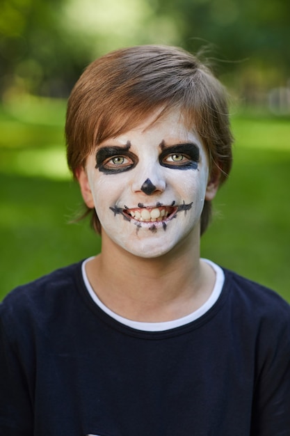 Tête et épaules portrait d'adolescent souriant portant un costume d'Halloween avec de la peinture pour le visage et tout en posant à l'extérieur