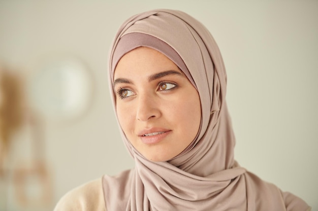 Tête et épaules portrait en gros plan d'une jeune femme musulmane adulte portant un hijab rose pâle regardant loin