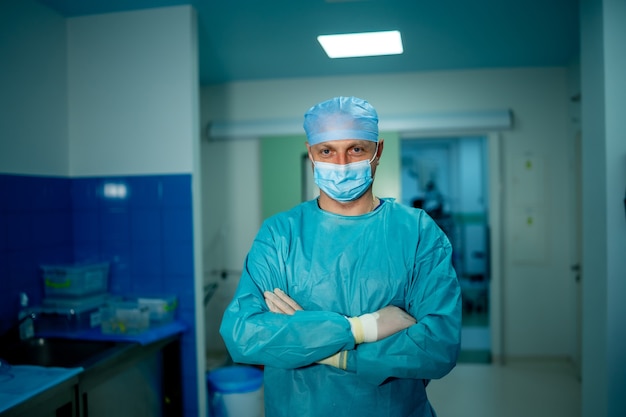 Tête et épaules portrait d'un médecin de sexe masculin portant un masque de protection et regardant la caméra posant sur fond de chambre d'hôpital.