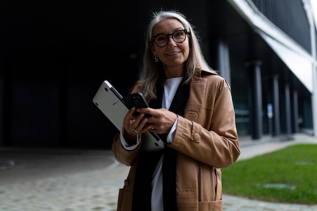 La tête de femme aînée avec un ordinateur portable dans des ses mains regarde l'appareil-photo dans la perspective d'un