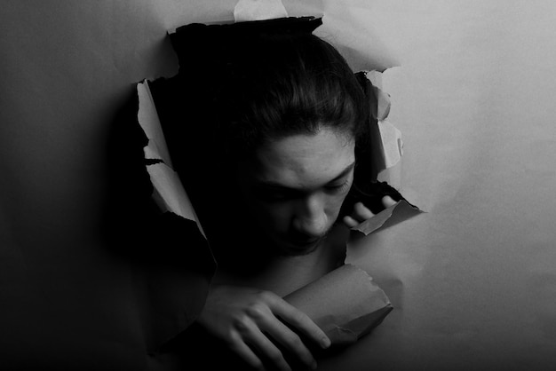 La tête de l'homme sortant et regardant à travers un trou de papier avec ses mains poussant le papier de côté
