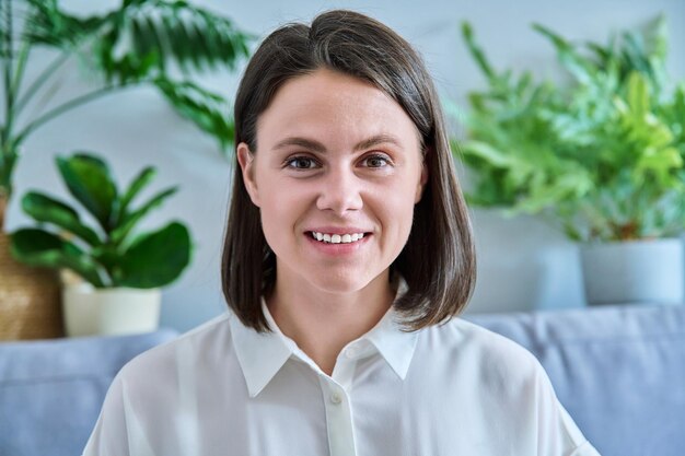 Tête jeune femme souriante regardant la caméra à l'intérieur de la maison