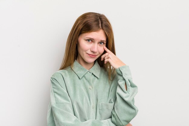 Tête rouge jolie femme gardant un œil sur vous ne faisant pas confiance en regardant et en restant alerte et vigilante