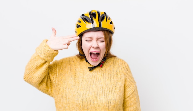 Tête rouge jolie femme à la recherche de geste de suicide malheureux et stressé faisant signe de pistolet concept de cyclisme