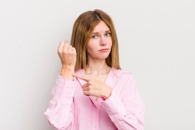 Tête rouge jolie femme à la recherche d'impatience et de colère pointant vers la montre demandant la ponctualité veut être à l'heure