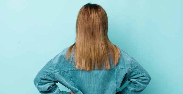 Tête rouge jolie femme se sentant confuse ou pleine ou des doutes et des questions se demandant avec les mains sur les hanches vue arrière