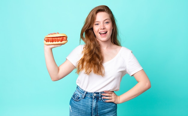 Tête rouge jolie femme semblant heureuse et agréablement surprise et tenant un hot-dog