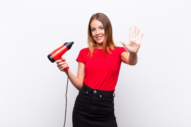 Tête rouge jolie femme souriante et sympathique, montrant le numéro cinq ou cinquième avec la main vers l'avant, compte à rebours tenant un coiffeur