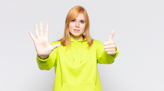 Tête rouge jolie femme souriante et à la sympathique, montrant le numéro six ou sixième avec la main vers l'avant, compte à rebours