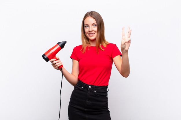 Tête rouge jolie femme souriante et à la sympathique, montrant le numéro trois ou troisième avec la main en avant, compte à rebours tenant un coiffeur