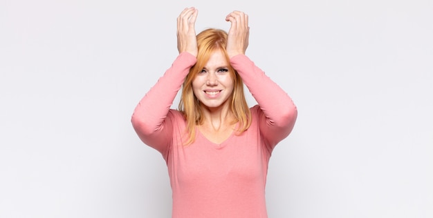 Tête rouge jolie femme stressée et anxieuse, déprimée et frustrée par un mal de tête, levant les deux mains à la tête