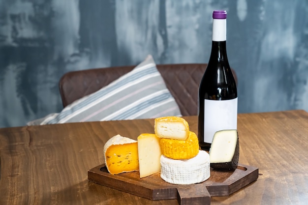 Têtes de fromages assorties sur une planche à découper et une bouteille de vin sur une table en bois. une fromagerie avec un café.