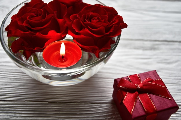 Têtes de roses et une bougie allumée dans un bol avec de l'eau et une boîte-cadeau sur un bois blanc. Concept de la Saint-Valentin