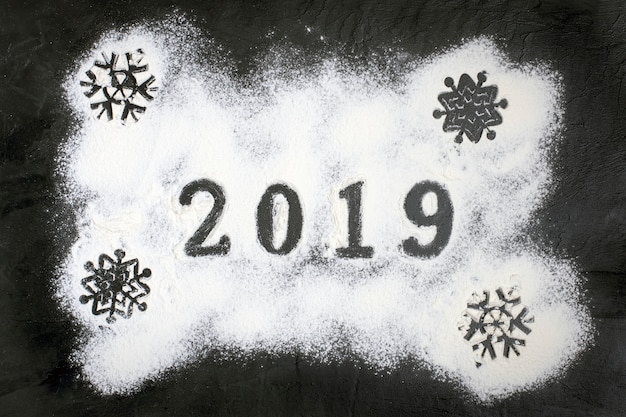 Texte de 2019 fait avec de la farine avec des décorations sur fond noir. Joyeux Noël, H