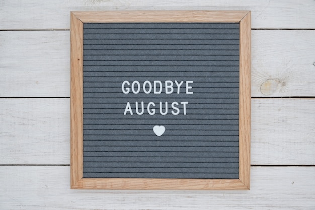 Texte en anglais au revoir août et un signe de coeur sur une planche de feutre gris dans un cadre en bois.