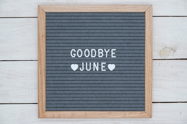 Texte en anglais au revoir juin et un signe de coeur sur une planche de feutre gris dans un cadre en bois.