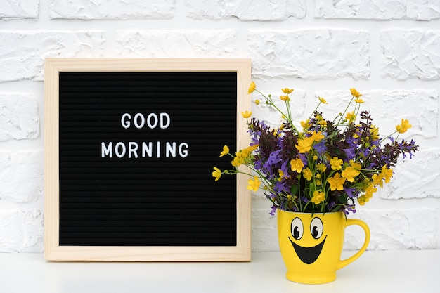 Photo texte bonjour sur tableau noir et bouquet de fleurs colorées dans une tasse jaune