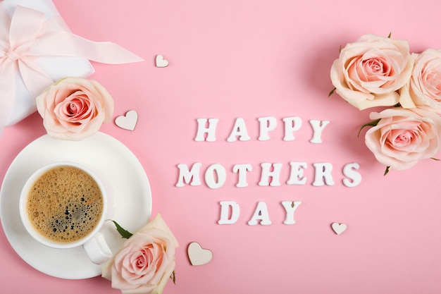 Photo texte de bonne fête des mères avec tasse de café, roses et cadeau sur fond rose
