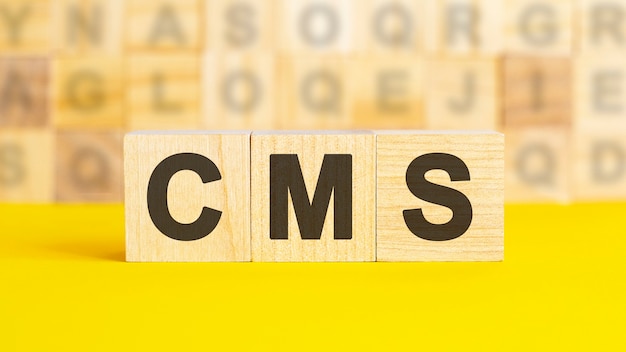 Le texte cms est écrit sur des cubes en bois sur une surface jaune vif. En arrière-plan se trouvent des rangées de cubes avec des lettres différentes. Concept d'entreprise. cms - abréviation de Content Management System