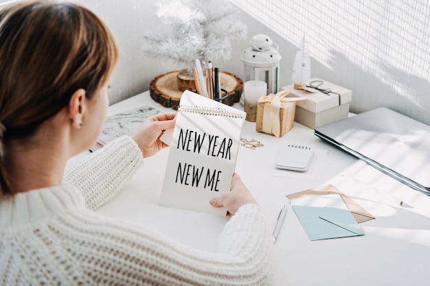 Texte du nouvel an nouveau moi dans le bloc-notes ouvert dans la main de la femme sur la table à la maison fixant des objectifs et du nouvel an