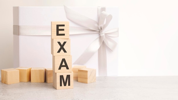 Le texte de l'examen est disposé dans une pyramide de cubes en bois à l'arrière-plan est une boîte cadeau en papier avec un ruban blanc brillant