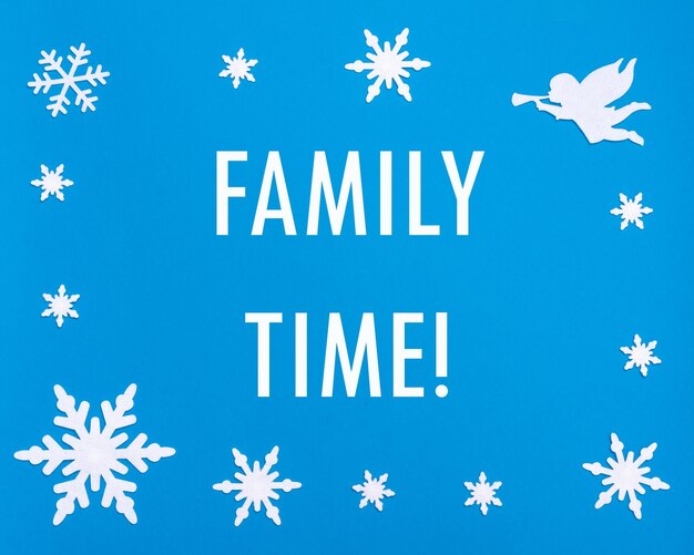 Photo texte family time sur fond bleu avec des flocons de neige de noël un ange blanc jouant de la trompette