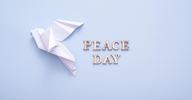 Texte de la journée de la paix à partir de lettres en bois avec colombe en papier blanc dans la main féminine sur fond bleu Concept de la journée internationale de la paix Photo verticale