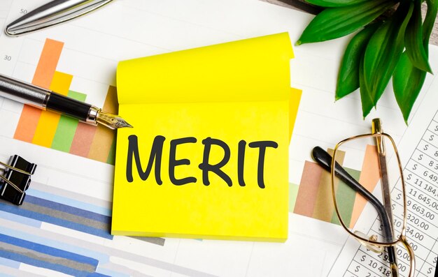 Texte MERIT sur un autocollant avec des tableaux, des verres et un stylo