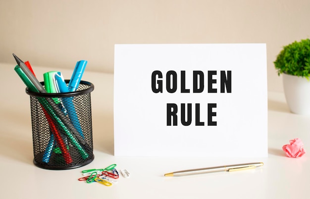 Le texte RÈGLES D'OR est écrit sur une feuille de papier pliée blanche sur la table. A proximité se trouvent des stylos et des crayons.