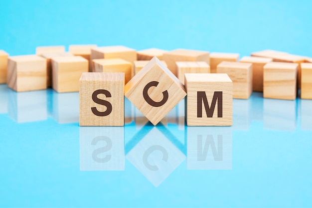 Le texte SCM Supply Chain Management écrit sur les cubes en bois en lettres noires les cubes sont situés sur un mot de concept de surface en verre bleu vif formant avec des cubes sur fond