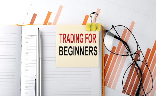 Texte TRADING FOR BEGINNERS sur l'autocollant sur le bloc-notes sur l'arrière-plan du diagramme