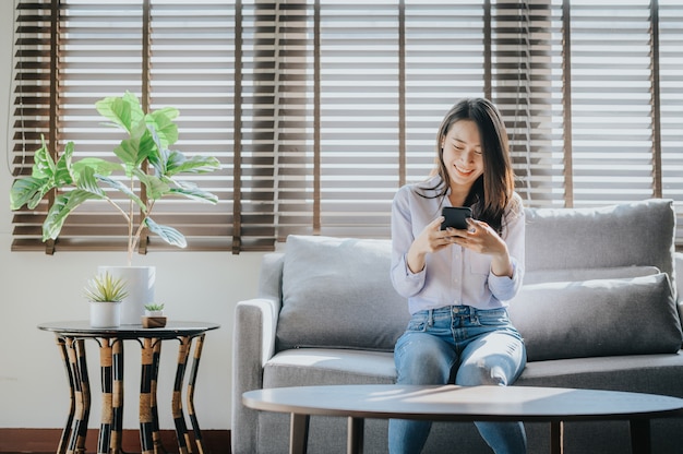 Textos de femme heureuse sur le smartphone assis sur le canapé