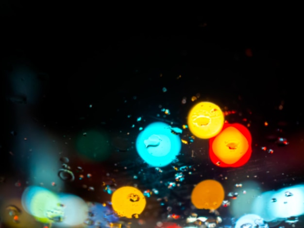 Texture floue de gouttes de pluie sur la fenêtre de la voiture avec fond abstrait bokeh coloré sur la route