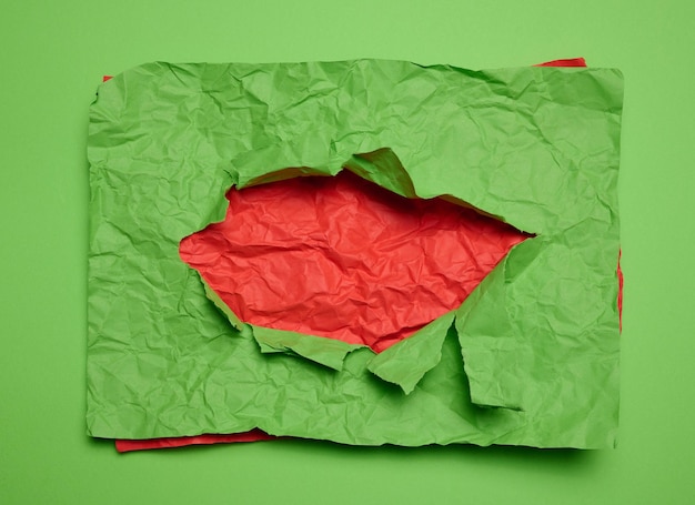 Texture de papier vert froissé avec trou déchiré et fond rouge