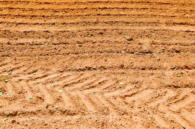 La texture de la terre brune de la route de sable avec des traces des bandes de roulement des pneus de la voiture du tracteur