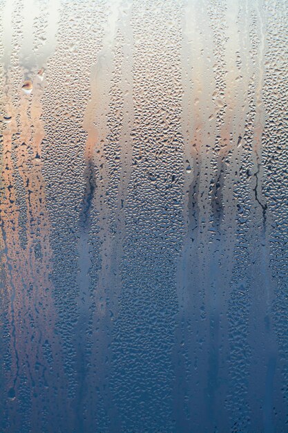 la texture tombe sur le verre sur le fond de l'aube du soleil bleu orange vif en couleurs