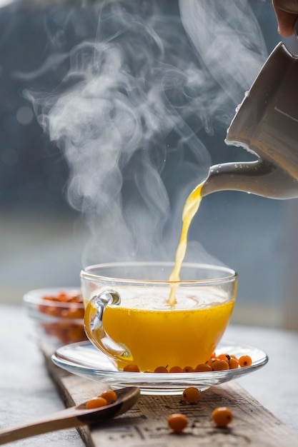 Thé à L'argousier Dans Une Tasse En Verre Devant La Fenêtre. Boisson Vitaminée Aux Herbes