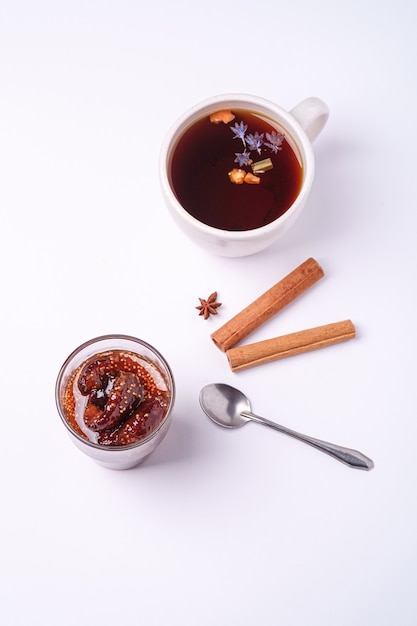 Thé aromatique noir chaud près de la confiture de figues, ambiance de petit-déjeuner de Noël à l'anis et à la cannelle sur fond blanc, vue d'angle