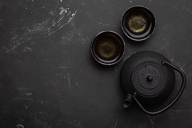 Thé asiatique traditionnel dans une théière vintage en fonte noire avec deux tasses sur une table en pierre sombre, vue de dessus. Mise à plat de l'ensemble d'arrangements de la cérémonie du thé asiatique, espace pour le modèle de texte