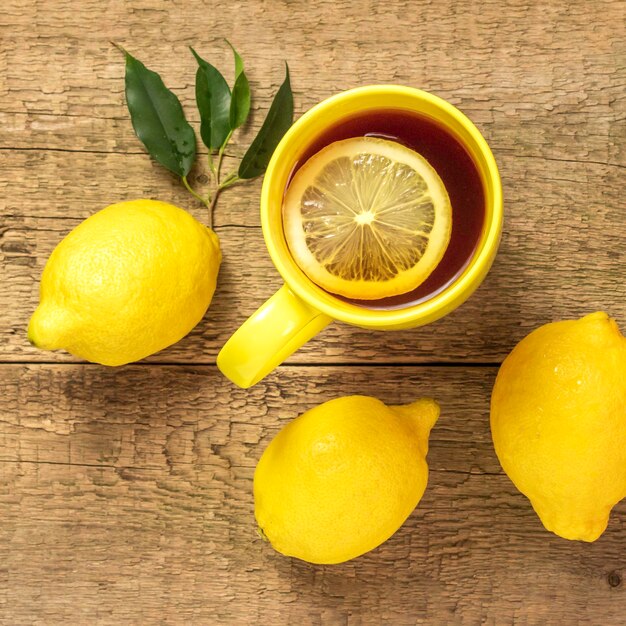 Thé au citron dans une tasse jaune sur fond de bois et citrons fraisVue de dessus