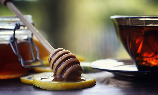 Thé au citron et à la menthe dans la nature. Une tasse de thé à la menthe chaud avec du citron et du miel en pot. Tranches de citron et une cuillère avec du miel pour du thé chaud.